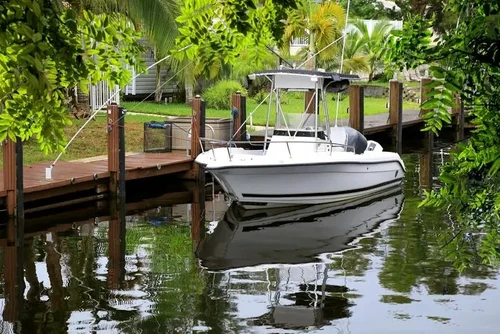 White center console boat docked at a private residential sweet water canal dock surrounded by vegetation.