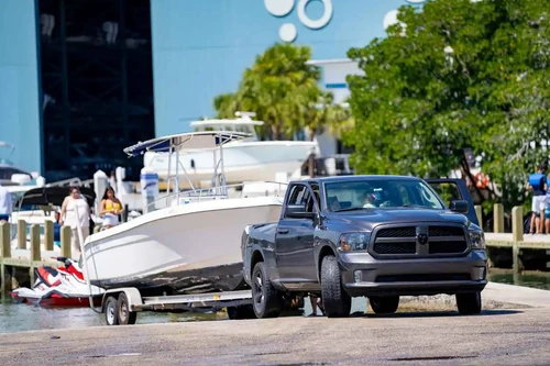 Gray Ram 1500 truck towing a white boat on a trailer at a marina boat ramp.