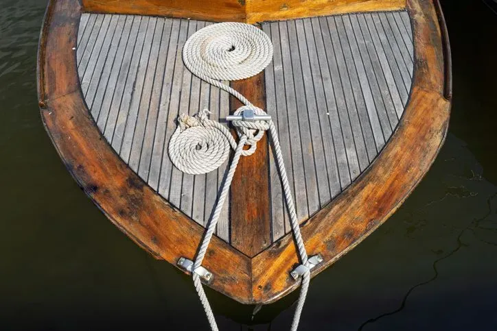 Overhead view of a wooden boat bow with coiled mooring ropes tied to a cleat.