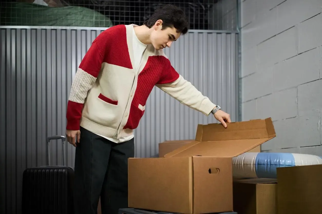 College student packing boxes and a suitcase into a self-storage unit for winter break between semesters.